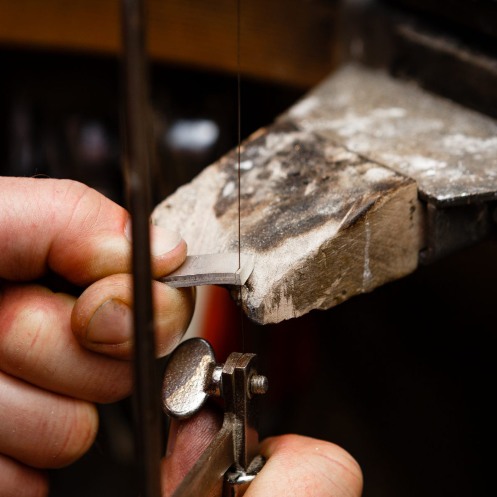 Detailaufnahme eines Goldschmieds bei der präzisen Handarbeit an einem Trauring. Der Fokus liegt auf der hochwertigen Fertigung von Memoire Eternity-Ringen, die für zeitlose Eleganz und exzellente Handwerkskunst stehen.