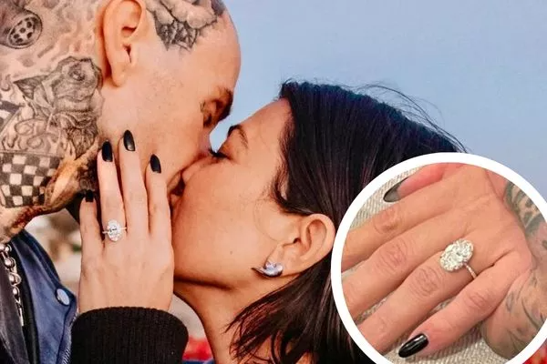 Kourtney Kardashian und Travis Barker teilen einen romantischen Moment, während Kourtney ihren atemberaubenden ovalen Verlobungsring präsentiert. Der Ring strahlt Eleganz und Raffinesse aus. Sie können diesen wunderschönen Verlobungsring bei NÓIR.com kaufen – wahlweise mit natürlichen oder labgrown Diamanten, garantiert zum besten Preis. Perfekt für Paare, die Luxus und Nachhaltigkeit in ihrem besonderen Moment verbinden möchten.