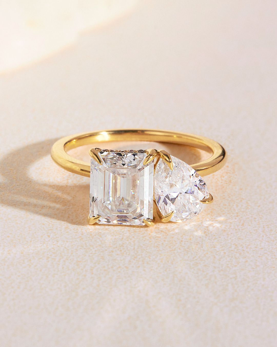 Eleganter Toi-et-Moi-Verlobungsring aus Gelbgold mit einem rechteckigen Emerald-Cut lab-grown Diamanten und einem natürlichen tropfenförmigen Diamanten. Ein einzigartiges Design, das Nachhaltigkeit und zeitlose Romantik miteinander verbindet.