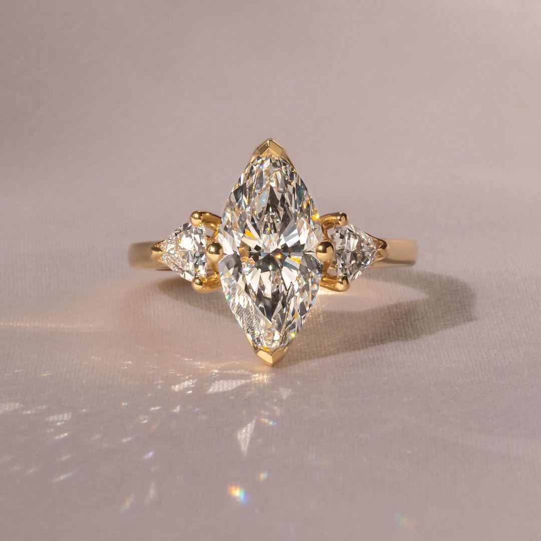 Eleganter Verlobungsring mit einem Marquise-Cut-Diamanten aus nachhaltigen lab-grown Diamanten, flankiert von zwei natürlichen Diamanten im Trillion-Cut, eingefasst in hochwertigem Gelbgold. Ein perfektes Schmuckstück für umweltbewusste Eleganz und zeitlose Schönheit.